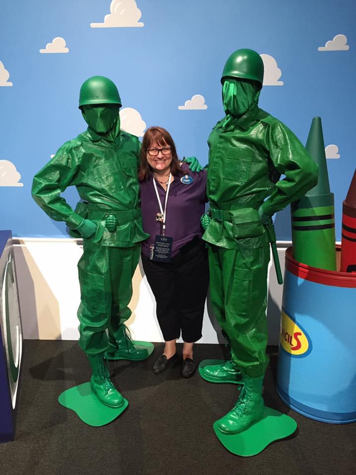 Tammy Vallario smiles standing next to two toy soldiers from Toy Story